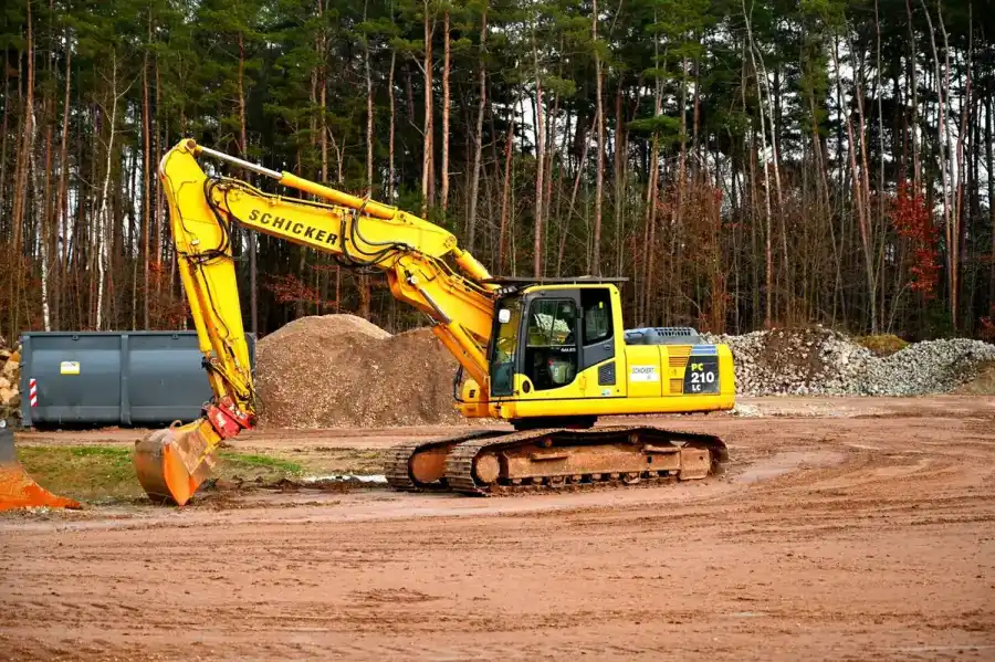 Yellow excavator sitting on freshly stripped ground at the edge of a stand of timber